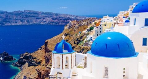 Breathtaking view of the Greek islands with whitewashed houses, crystal-clear waters, and a traditional sailboat. Discover the best of Greece with Grand Voyages tour packages.